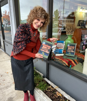 Woman with curly hair in a red top and black apron placing promotional flyers in a storefront window display.
