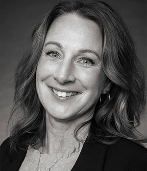 Portrait of a smiling woman with shoulder-length wavy hair, wearing a dark blazer in a professional headshot.